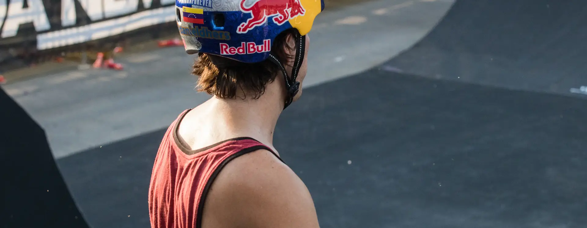 Person in a Red Bull helmet looking over a skate park ramp.